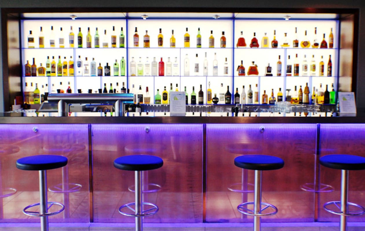 Mit LED-Lichttechnik beleuchtete Bar-Rückwand aus Lightpanel frameless cover mit Regalvorbau aus Iceplex von Designpanel.